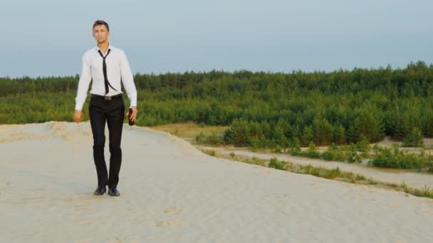 Young businessman with a bottle of alcohol is on the sand, weakens tie. Concept: go away from the problems, depression, bankruptcy — Stock Video