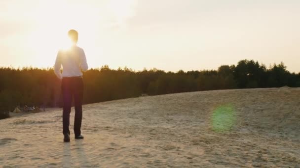 Un jeune homme d'affaires avec une bouteille d'alcool est sur le sable, affaiblit la cravate. Concept : s'éloigner des problèmes, de la dépression, de la faillite. Vue arrière — Video