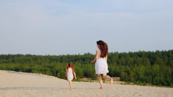 Mamá juega con su hija, corre a la arena. Vista trasera — Vídeo de stock