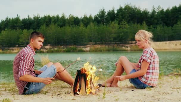 朋友的男人和一个女人正坐在篝火旁，烤棉花糖上枝. — 图库视频影像