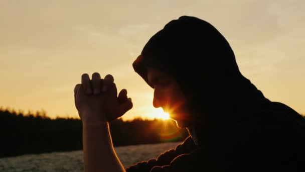 Dromer bij zonsondergang. Een jonge man zit in het profiel van de kap aan de camera. Hij is attent, de zonnestralen maken hun weg uit zijn gezicht — Stockvideo