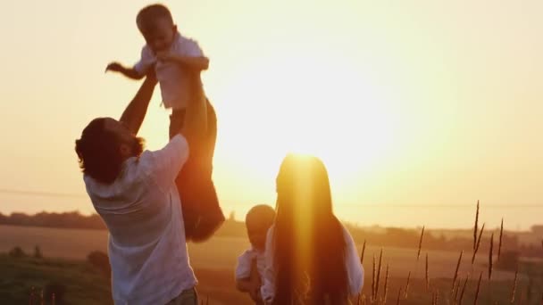 Eltern, die Spaß haben, mit den Kindern zu spielen. Vater und Mutter warfen Söhne über seinen Kopf in den Sonnenuntergang — Stockvideo