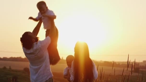 Genitori del divertimento giocando con i bambini. Papà e mamma gettato figli sopra la testa nel tramonto — Video Stock