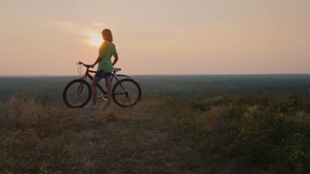 Kvinna som står nära en cykel ser ut vid solnedgången — Stockvideo