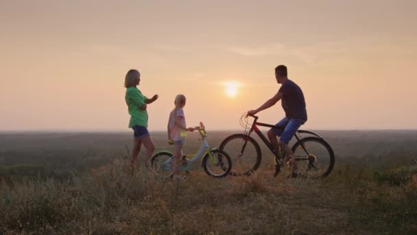 Família juntos admirando o pôr do sol, de pé ao lado de uma bicicleta — Vídeo de Stock