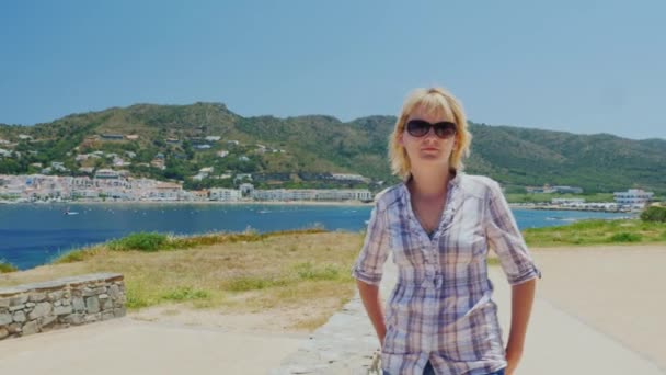 Steadicam-Aufnahme: Eine Touristin spaziert an der Küste entlang, vor dem Hintergrund eines mediterranen Dorfes mit Katakomben in Spanien — Stockvideo