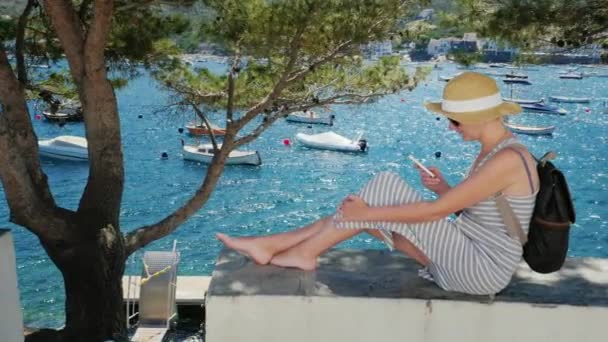 Jeune femme assise sur le fond de la baie avec des bateaux et des yachts. C'est taper quelque chose sur un smartphone — Video