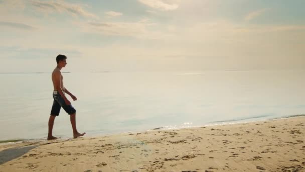 夕暮れ時のビーチに沿って歩いてティーンエイ ジャーの男の子。美しい夕暮れの空の背景 — ストック動画