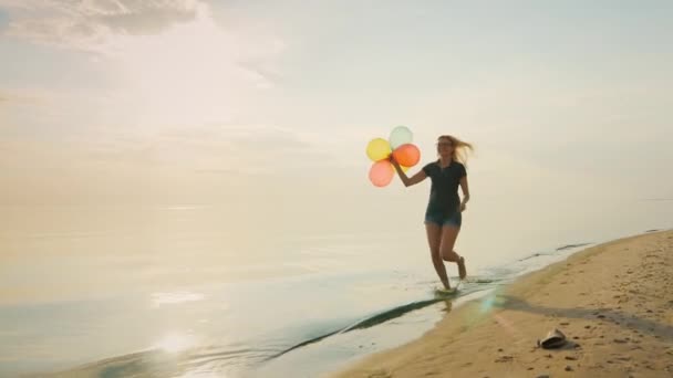 Mujer joven y despreocupada corriendo por la playa, sosteniendo globos en su mano. Concepto - la facilidad, la libertad, la alegría , — Vídeo de stock