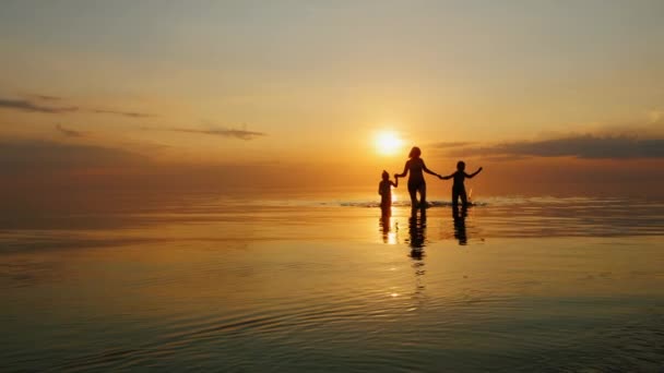Madre con dos hijos riendo en el mar al atardecer, fuera del agua — Vídeos de Stock