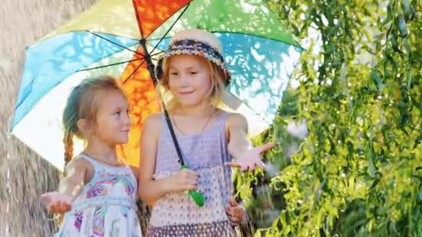 Dos niñas de 4 y 6 años de esconderse bajo coloridos paraguas. Lluvia cálida de verano, los niños son felices — Vídeos de Stock