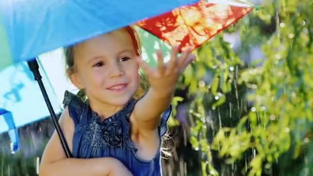 Porträt eines unbeschwerten Mädchens, das den Regen genießt. Es sollte unter dem Dach der Regenbogenfarbe sein — Stockvideo