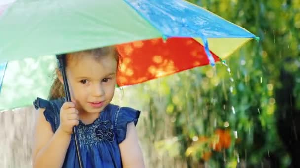 Веселая маленькая девочка, три года стоящая под зонтиком, под дождем — стоковое видео