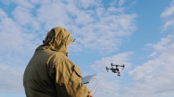 O homem controla o drone, que está flutuando no ar ao seu redor contra o fundo do céu azul — Vídeo de Stock
