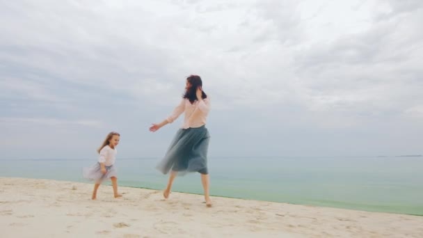 Young mother plays with her daughter three years. He catches her and circling around him in the sea and sky background — Stock Video