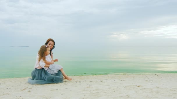 Junge Mutter mit einem Mädchen von drei Jahren sitzt am Strand und plaudert — Stockvideo