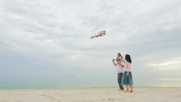 娘と遊ぶフレンドリーな若い家族は、凧を飛ばします。美しい海と空を背景に — ストック動画