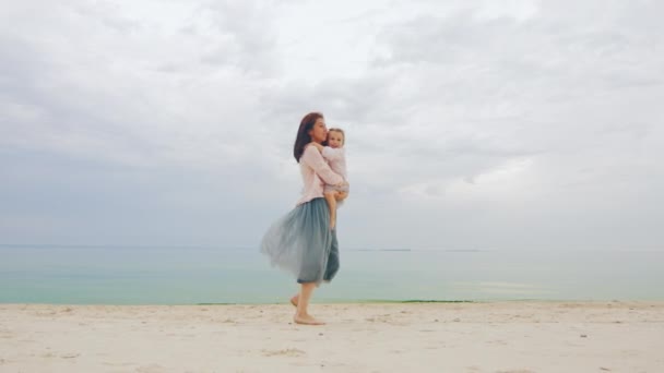 Mutter spielt mit ihrer Tochter drei Jahre, zusammen lachen, kreisen auf seinen Händen und werfen. vor dem Hintergrund von Meer und Himmel — Stockvideo