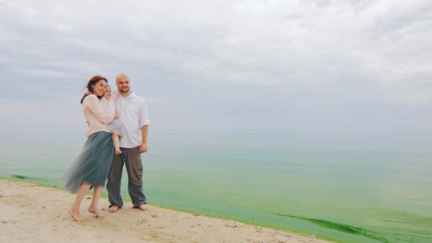 Молодая семья из трех человек позирует для фотографии на фоне моря — стоковое видео