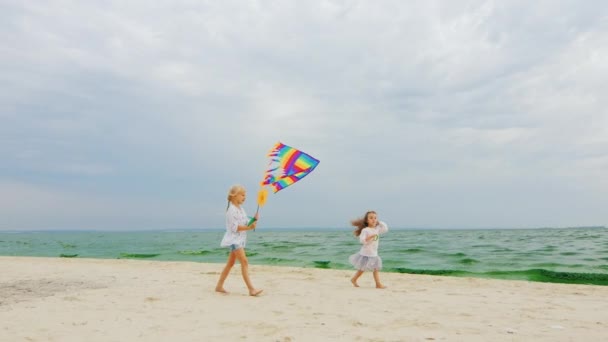 Dos niños jugando con una cometa en la playa en el fondo del mar y el cielo — Vídeos de Stock