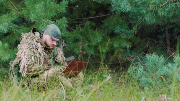 En man i militära Uniform sitter i skogen njuter av den bärbara datorn — Stockvideo