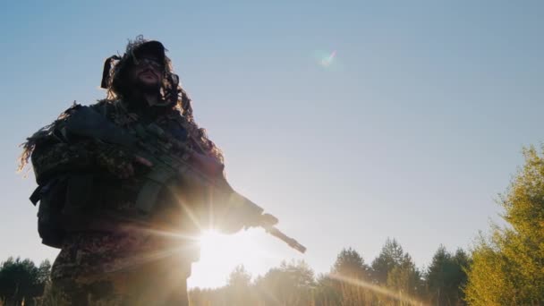 Солдат в американских боеприпасах стоит против неба. Солнце светит ему на руки. Стрельба под низким углом — стоковое видео