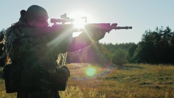 Ein Soldat in Tarnkleidung mit Gewehr geht nach vorne und blickt durch das Zielfernrohr. Siluluet, die Sonnenstrahlen scheinen durch die Arme — Stockvideo
