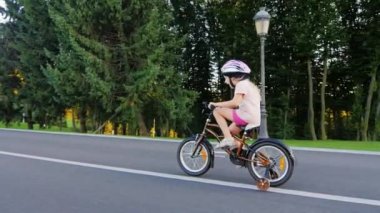 Steadicam çekim: Komik kız beş yaşında ekstra tekerlekler gülümseyerek bir bisiklet sürme