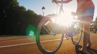 Bir kadın bisiklete biner. Resimde, bir bacaklar ve tekerlek görebilirsiniz, güneş ışınları bisiklet ile parlaklık