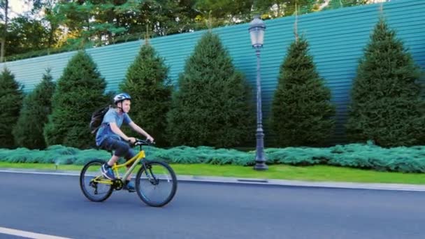 El adolescente trece monta una bicicleta a lo largo de una cerca verde — Vídeos de Stock