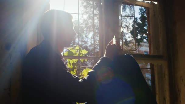 Un joven se sienta en una casa abandonada. En las manos sosteniendo una jeringa. Concepto: la fuerza de voluntad para dejar las drogas — Vídeo de stock