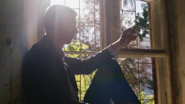 Junger Mann mit einer Spritze in der Hand. In einem verlassenen Haus in der Sonne sitzen. Suchtgefahr — Stockvideo