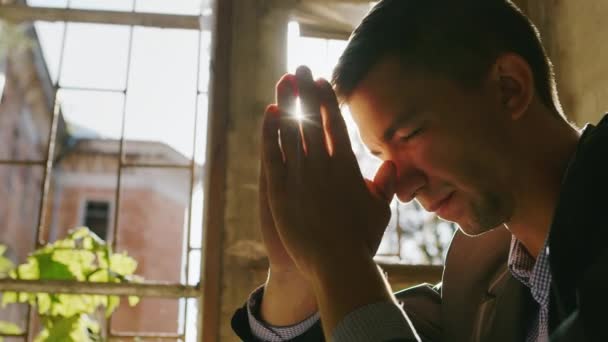 Portret van een jongeman die in de zon bidt. Zittend bij het raam in een oud gebouw — Stockvideo