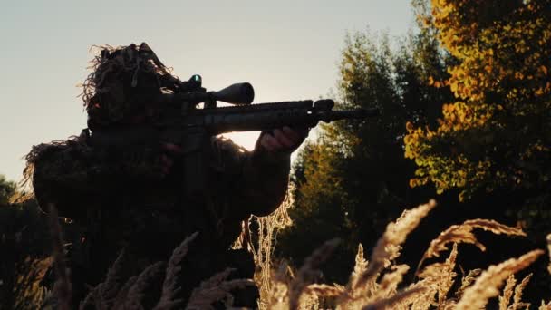 Sniper i kamouflage kläder tar sikte. Solens strålar lyser igenom i ryggen och armarna — Stockvideo