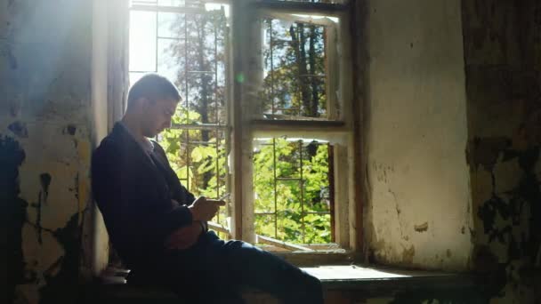 Unhappy young businesswoman writing sms. Sitting in an abandoned house near the window. Concept: bankruptcy, crash, divorce and loneliness — Stock Video