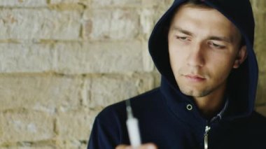 Uyuşturucuyu bırakma iradesi. Şırıngaya bakan kapüşonlu bir genç.