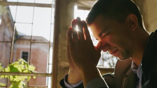 Portrait d'un jeune homme priant au soleil. Assis près de la fenêtre dans un vieux bâtiment — Video