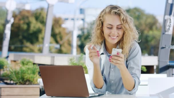 Joven atractiva mujer de negocios que trabaja en un café. Utiliza el teléfono y el portátil — Vídeo de stock