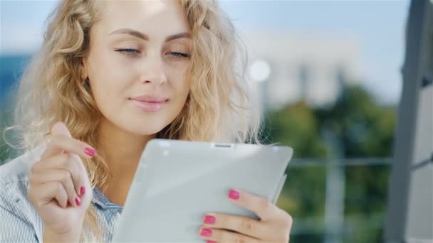 Ritratto di una giovane donna attraente utilizza tablet su una zona estiva nel caffè. Sorrisi, emozioni positive — Video Stock