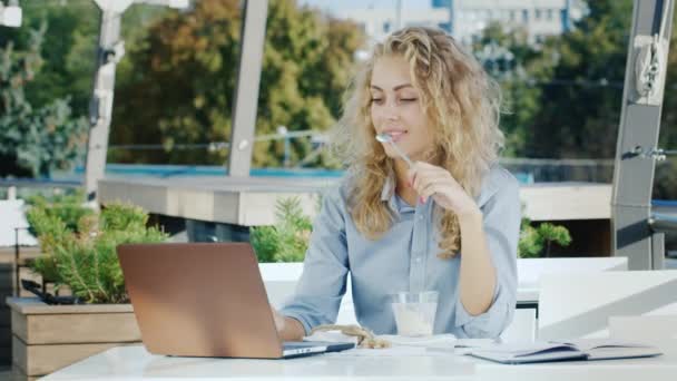 Młoda biznesmenka pracująca w kawiarni na letniej ziemi. Je lody, używa laptopa. — Wideo stockowe