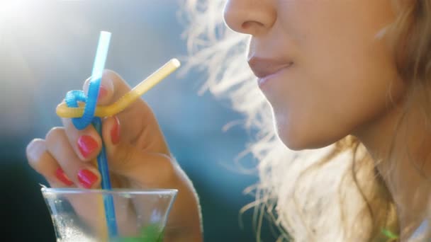 Young woman stirs the drink in the glass. In the picture visible lips and hair in which the sun shines. The concept - a heavenly vacation — Stockvideo