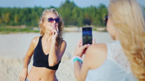 Mujer fotografiando a su novia en la playa. Usar teléfono celular — Vídeos de Stock