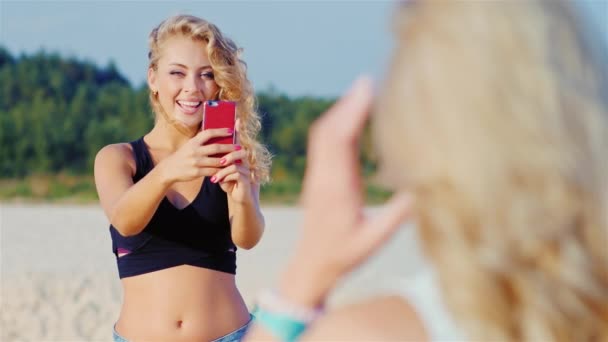 Mujer atractiva joven con un teléfono inteligente fotos de su novia en la playa — Vídeos de Stock