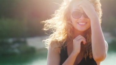 Denize karşı güneşte kameraya gülümseyen çekici bir genç kadın portresi. Rüzgar ve güneş saçlarıyla oynuyor.