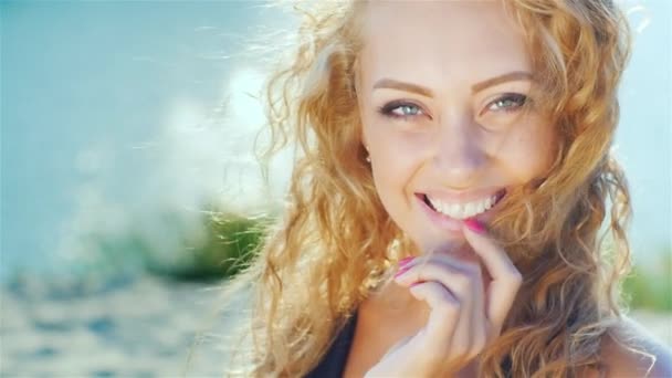 Gros plan d'une belle jeune femme souriant à la caméra. Journée ensoleillée à la plage près de la mer — Video