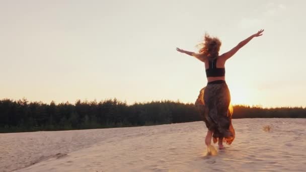 Mujer joven en una hermosa luz de vestido corre a lo largo de la playa hasta el atardecer. Estirando los brazos al sol. Concepto - la energía de la juventud, la salud, los sueños, la libertad — Vídeo de stock