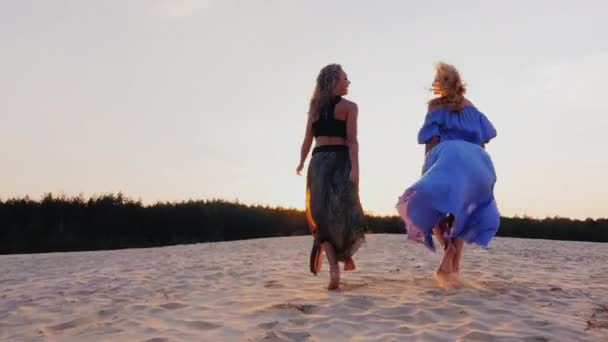 明るい風通しの良いドレスを着た二人の若い女性が太陽に向かって走ります。概念:自由、女性の夢、健康、若さ、エネルギー — ストック動画