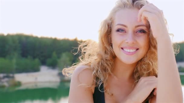 Joven mujer hermosa sonriendo a la cámara. Posando en el fondo de los pintorescos lagos y bosques — Vídeos de Stock