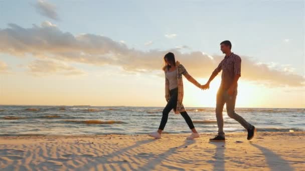 Steadicam shot: Loving couple walking at sunset on the beach or lake. She leads the guy flirting — Stock Video