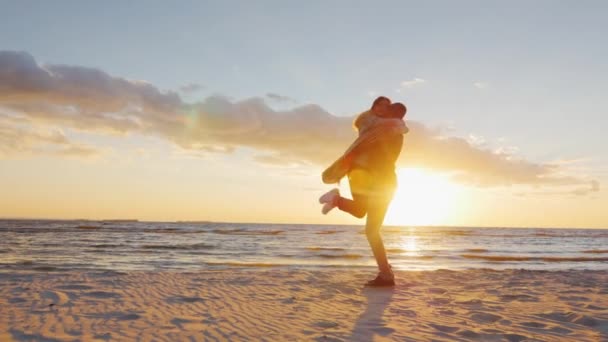 Paar in liefde plezier hebben op het strand bij zonsondergang berugegu. De man draait om hem zijn vriendin. Concept-de huwelijksreis, liefde, jeugd — Stockvideo